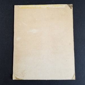 May include: A blank, off-white card with a light brown border. The card has a piece of tape on the top edge.
