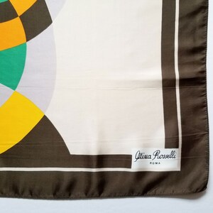 May include: A square silk scarf with a geometric design. The scarf features a cream-colored background with a brown border and accents. The design includes yellow, green, and black shapes. The label reads "Olivia Rosselli ROMA."