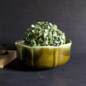 May include: A green ceramic planter with a scalloped rim. The planter is filled with a small, round, green artificial plant.