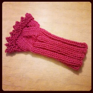 May include: A pink knitted wrist warmer with a decorative ruffled edge.
