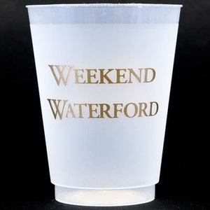 May include: A translucent white plastic cup with the words "WEEKEND WATERFORD" printed in gold. The cup has a slightly flared shape and a small base. The text is centered on the cup.