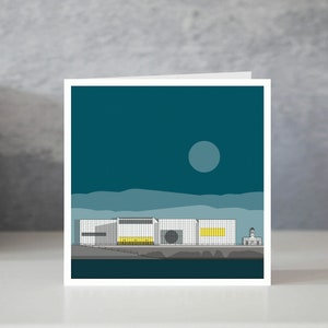 May include: Greeting card featuring a minimalist illustration of a modern building complex under a teal night sky with a full moon. The buildings have white facades with yellow-lit windows. A small church-like structure is also visible.