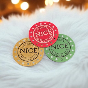 May include: Three circular tags featuring the text S. CLAUS OFFICIAL NICE LIST. One tag is red with white dots, one is green with white dots, and one is gold with a textured surface. Each tag has a scalloped border and a central NICE inscription.