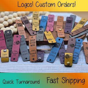 May include: A selection of leather tags in various colours, including pink, blue, and brown, with custom logos and text. The tags are rectangular with rounded edges and feature the text "Logos! Custom Orders!"