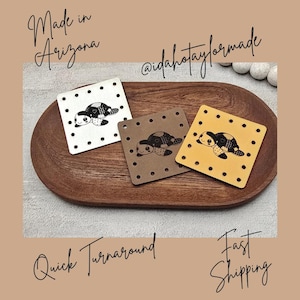 May include: Three square coasters with a turtle design, each with a different background color: white, brown, and yellow. The coasters are arranged on a wooden tray. The text "Made in Arizona" and "@idahotaylorformade" are visible.