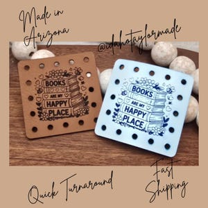 May include: Two square leather-like patches with pre-punched holes along the edges. One patch is tan with black text and the other is light blue with dark blue text. Both feature a stack of books with the text BOOKS ARE MY HAPPY PLACE.