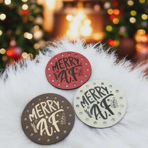 May include: Three round coasters with the text "MERRY AF" in a handwritten style. The coasters are red, brown, and off-white, each with a different background color. Each coaster has small, evenly spaced holes around the edge.