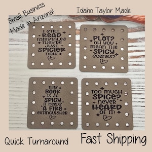 May include: Four square taupe leather-like coasters with pre-punched holes along the edges. Each coaster features dark brown laser-engraved text about spicy books, including phrases like I still read fairytales, they're just spicier now, and Plot? Oh you mean the spicy scenes?