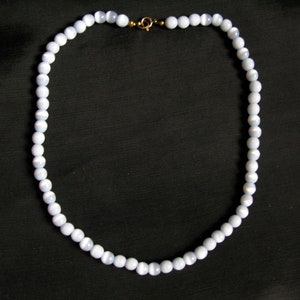 May include: A delicate necklace featuring light blue, round beads. The beads are strung together, forming a complete circle. The necklace is secured with a gold-colored clasp. The beads appear to be approximately 0.25 inches in diameter.