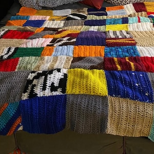 May include: A large, rectangular crochet blanket composed of numerous square patches in a wide variety of colors including red, blue, yellow, green, black, white, and brown. The squares feature diverse textured stitch patterns and yarn weights.