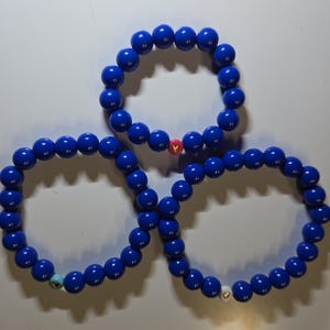 May include: Three blue beaded bracelets with small heart charms in gold, white, and pink.