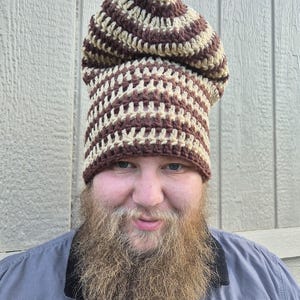 May include: A slouchy crochet beanie featuring a repeating horizontal striped pattern in alternating dark brown and cream yarn. The hat has a textured, open-stitch construction with a rounded top and a fitted band that sits around the head.