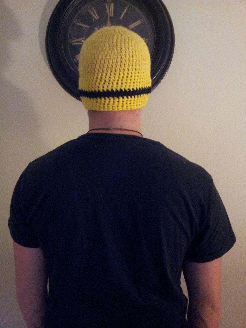 May include: A yellow crocheted beanie with a black stripe around the brim. The beanie is being worn by a person.