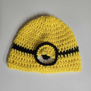 May include: A yellow crocheted hat with a black stripe and a single eye, resembling a Minion character.