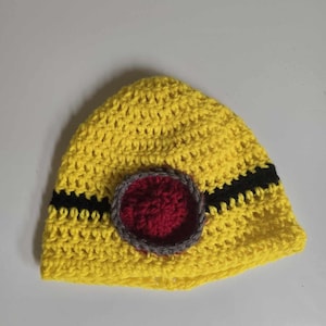 May include: A yellow crocheted beanie with a black and red circle design.