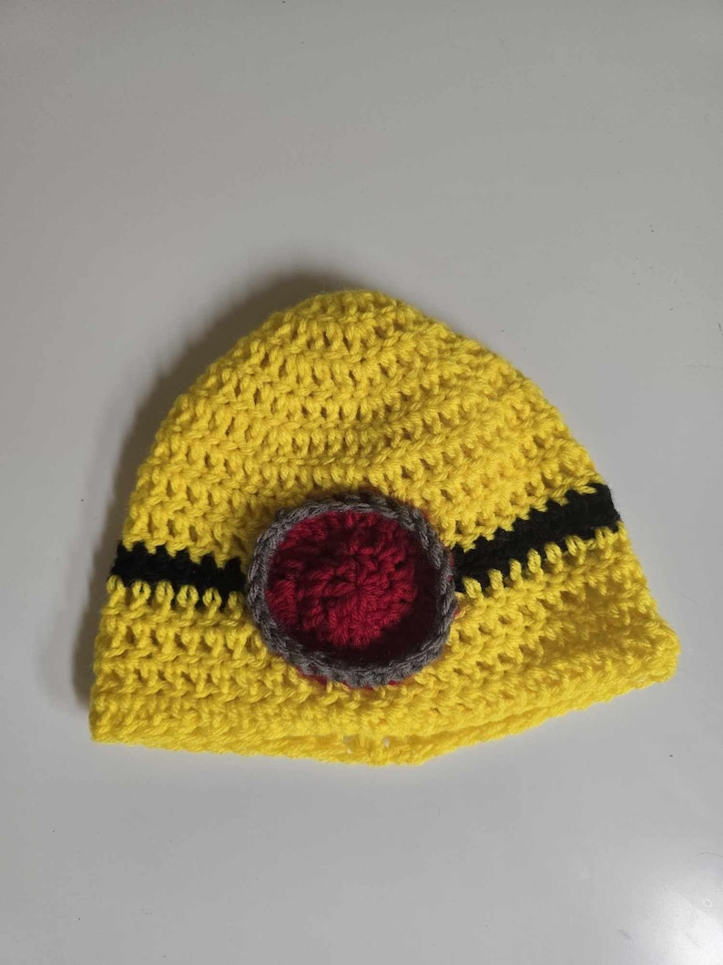 May include: A yellow crocheted beanie with a black and red circle design.