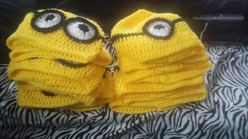 May include: A stack of yellow crocheted hats with black and white details resembling a minion character.
