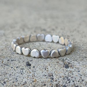 May include: A silver ring with a band of small, connected heart shapes.