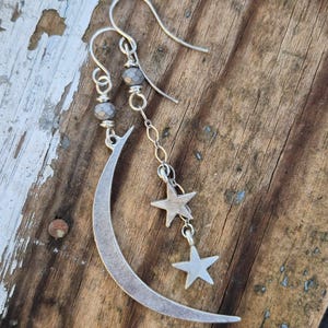 May include: Silver crescent moon earrings with two dangling star charms and gray beads.