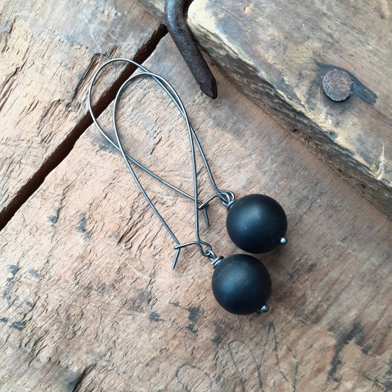May include: A pair of black dangle earrings with black round beads. The earrings have a simple design and are made of metal.