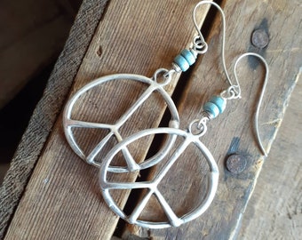 May include: Silver peace sign earrings with turquoise beads. The earrings are dangling and have a simple design.