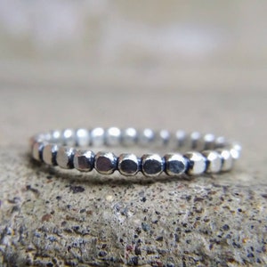 May include: A silver ring with a beaded design. The ring is made of small, round beads that are connected together to form a continuous band.