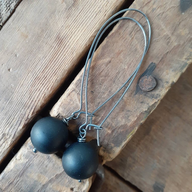 May include: A pair of black earrings with black bead accents. The earrings are made of thin silver wire.
