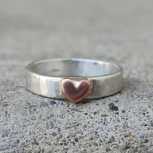 May include: A silver band ring with a hammered texture and a small copper heart in the center.