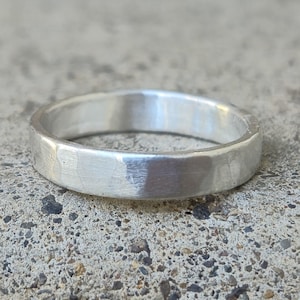 May include: A silver hammered band ring. The ring is made of a smooth, polished metal and has a textured surface.