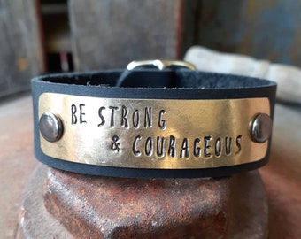 May include: Black leather bracelet with a gold metal plate that reads "BE STRONG & COURAGEOUS".