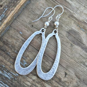 May include: Silver oval earrings with a hammered texture and a smooth bead at the top of the hook.