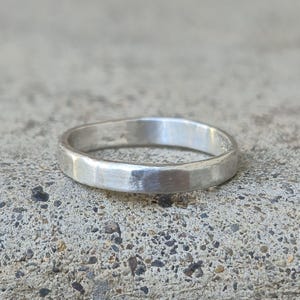 May include: A simple silver band ring with a hammered finish. The ring is smooth and has a matte finish.