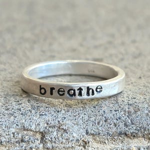 May include: A silver ring with the word "breathe" engraved on it.
