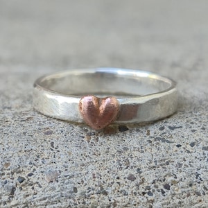 May include: A silver band ring with a hammered finish and a small copper heart accent.