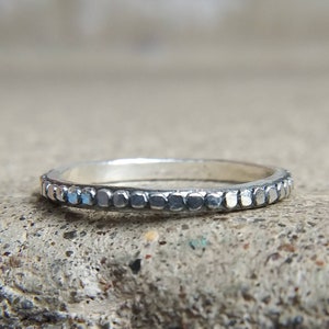 May include: A silver ring with a textured band. The band is decorated with a row of small, raised squares.