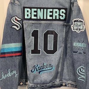 May include: A blue denim jacket with various patches, including a name patch that reads "BENIERS", a number "10", and a logo that says "Kraken Hockey".