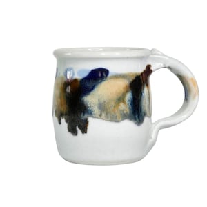 May include: White ceramic mug with a unique, abstract design. The mug features a rounded body and a curved handle. The design includes splashes of blue, brown, and tan colors. The mug is suitable for coffee, tea, or other beverages.