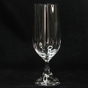 May include: A clear, stemmed champagne flute with a tall, slender bowl and a decorative base. The glass has vertical lines etched into the bowl. The glass is designed for serving sparkling wine or champagne.