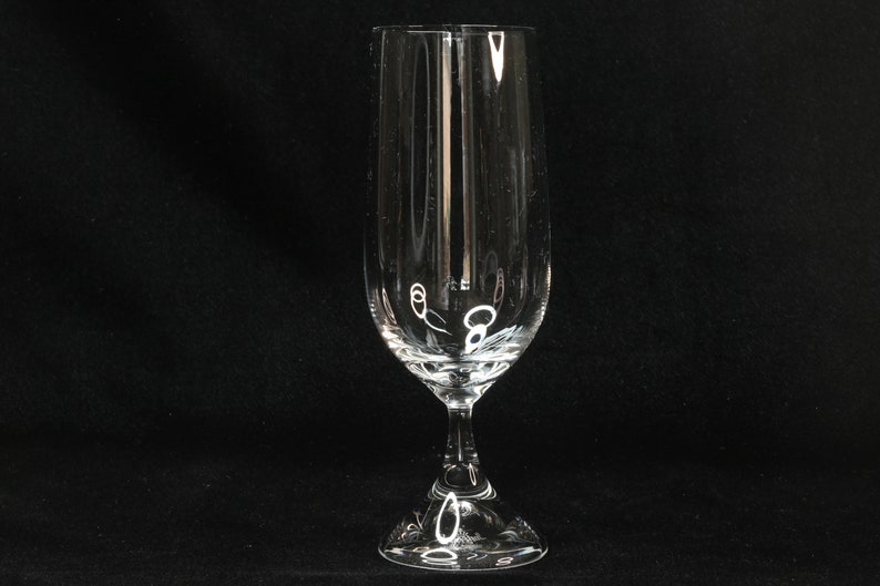 May include: A clear, stemmed champagne flute with a tall, slender bowl and a decorative base. The glass has vertical lines etched into the bowl. The glass is designed for serving sparkling wine or champagne.