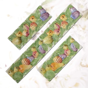 May include: Four rectangular ceramic serving dishes with a raised relief design of various fruits and green leaves. The fruits include pears, figs, and other colorful produce. The dishes are arranged diagonally.