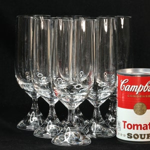 May include: A set of clear, stemmed champagne flutes with a decorative design near the base, next to a can of Campbell's Condensed Tomato Soup. The flutes are tall and slender, perfect for celebrations.
