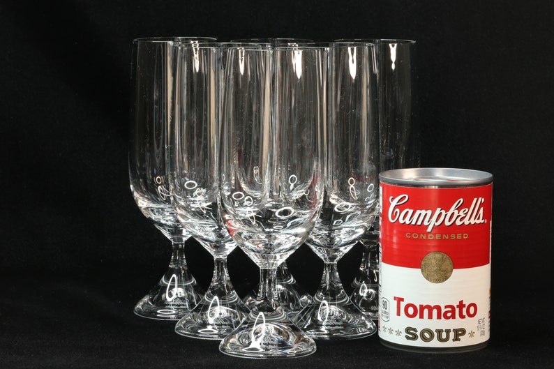 May include: A set of clear, stemmed champagne flutes with a decorative design near the base, next to a can of Campbell's Condensed Tomato Soup. The flutes are tall and slender, perfect for celebrations.