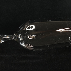 May include: A clear, stemmed champagne glass with a wide bowl and a slender stem. The glass has a decorative design near the top of the bowl. The glass is lying on its side against a black background.