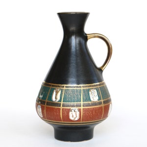 Op de afbeelding: Zwarte keramische vaas met een gouden handvat en een geometrisch ontwerp in tinten groen, goud en rood.