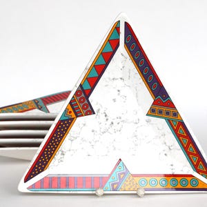 May include: A set of six triangular ceramic plates with a white background and colourful geometric patterns. The plates are stacked on top of each other.
