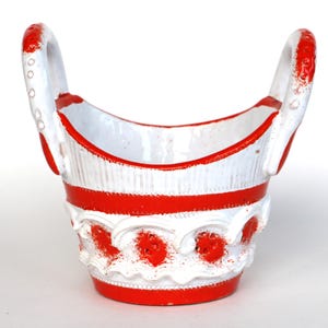 Op de afbeelding: Een witte keramische kom met rode strepen en decoratieve details. De kom heeft twee rode handvatten en een afgeronde vorm.