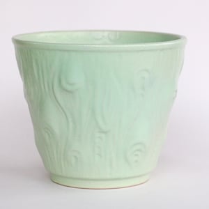 Op de afbeelding: Een lichtgroene keramische plantenpot met een getextureerd houtnerfmotief. De pot heeft een eenvoudige, klassieke vorm met een brede opening en een ronde bodem.