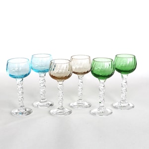 May include: Six colorful stemmed glasses with textured bowls and twisted stems. The glasses are in shades of blue, brown, white, and green. The glasses are arranged on a white background.