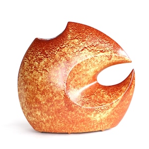 Op de afbeelding: Een unieke, abstracte keramische vaas met een afgeronde vorm en een grote, gebogen opening. De vaas heeft een textuur met een mix van oranje en gouden tinten, wat een warme, aardse uitstraling creëert. Het ontwerp is modern en sculpturaal.