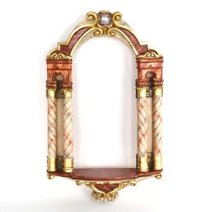 Op de afbeelding: Oornamentale, decoratieve wandplank in een boogvorm. De plank heeft twee zuilen met een crème- en rood marmereffect, gouden accenten en een rode plank. Bovenop is een heldere edelsteen geplaatst.